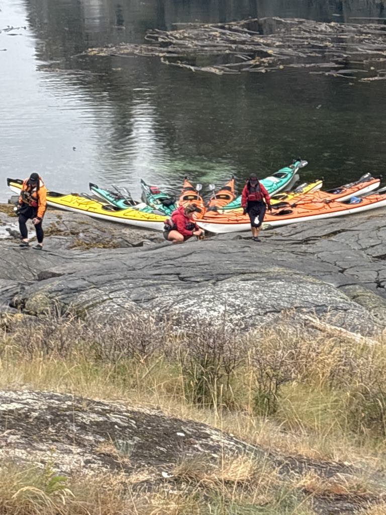 Bob Rein a group of people standing next to a boat on a river bank with kayaks on the shore