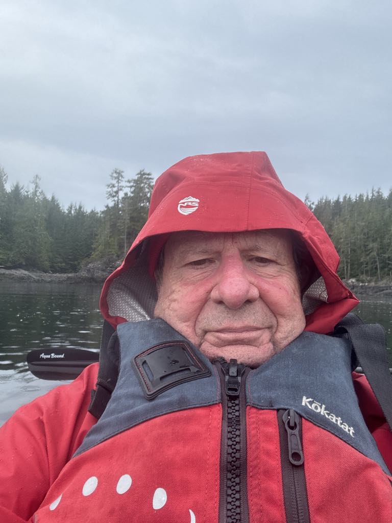 Bob Rein in a red jacket is in a boat on a lake with trees and a forest in the background