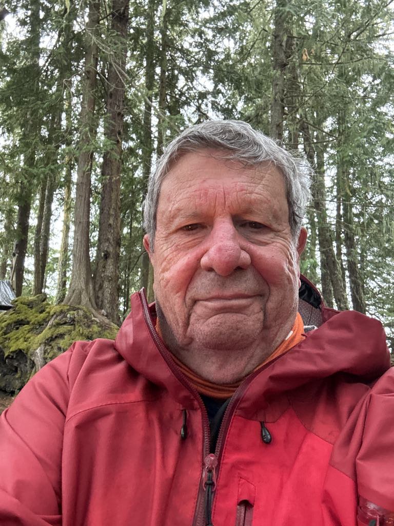 Bob Rein in a red jacket standing in front of a forest with trees