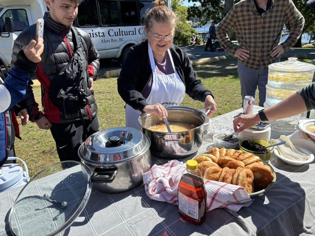 Bob Rein Reflections Off The Grid woman serving food at lively outdoor event with pots pastries and checkered tablecloth